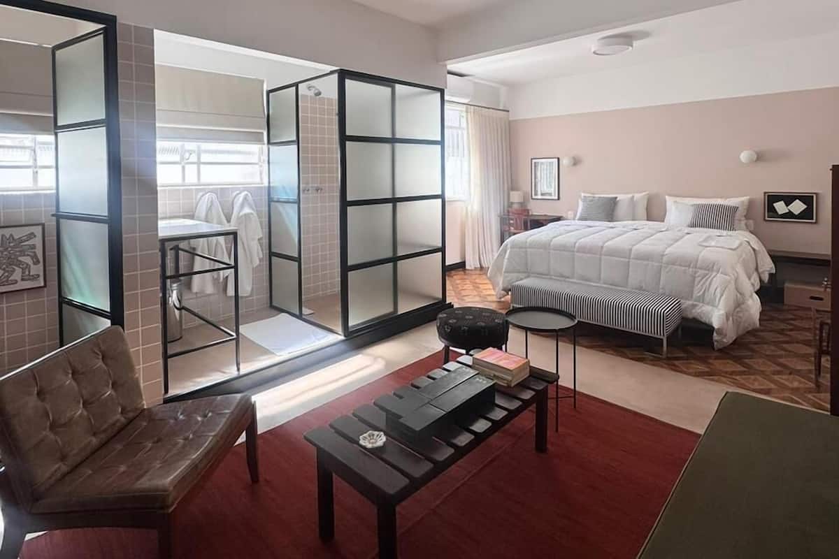 Ein modernes Hotelzimmer mit Bett, einer Sitzecke mit einer Bank, einem kleinen Tisch und einem großen Spiegel.