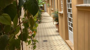 Un corredor cubierto con piso de baldosas, plantas en macetas y una serie de ventanas a lo largo de las paredes.