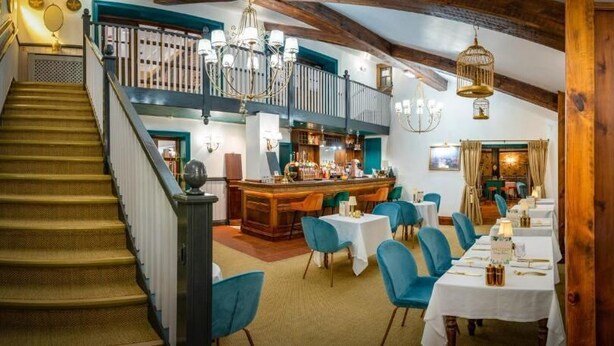 A restaurant with a staircase, bar, and dining area with blue chairs and white tables. - The millfield  (Broughton)