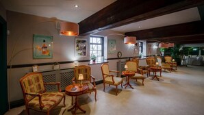 A hotel lobby with wooden chairs and tables, framed artwork on the walls, and a large window providing natural light. - The millfield  (Broughton)