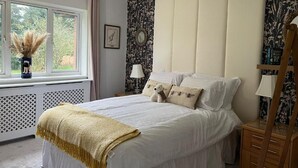 A bedroom with a large bed, a window with a view, a bedside table, and a lamp. - The millfield  (Broughton)