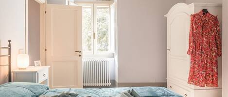 Un dormitorio con cama, radiador, armario y ventana.