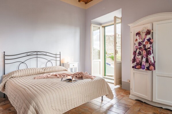 A bedroom with a bed, a nightstand, a wardrobe, and a door leading to an outdoor area. - Appartamento delle Volte (Cortona)