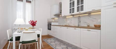 A modern kitchen with white cabinets, a marble countertop, and a dining area with a table and chairs.