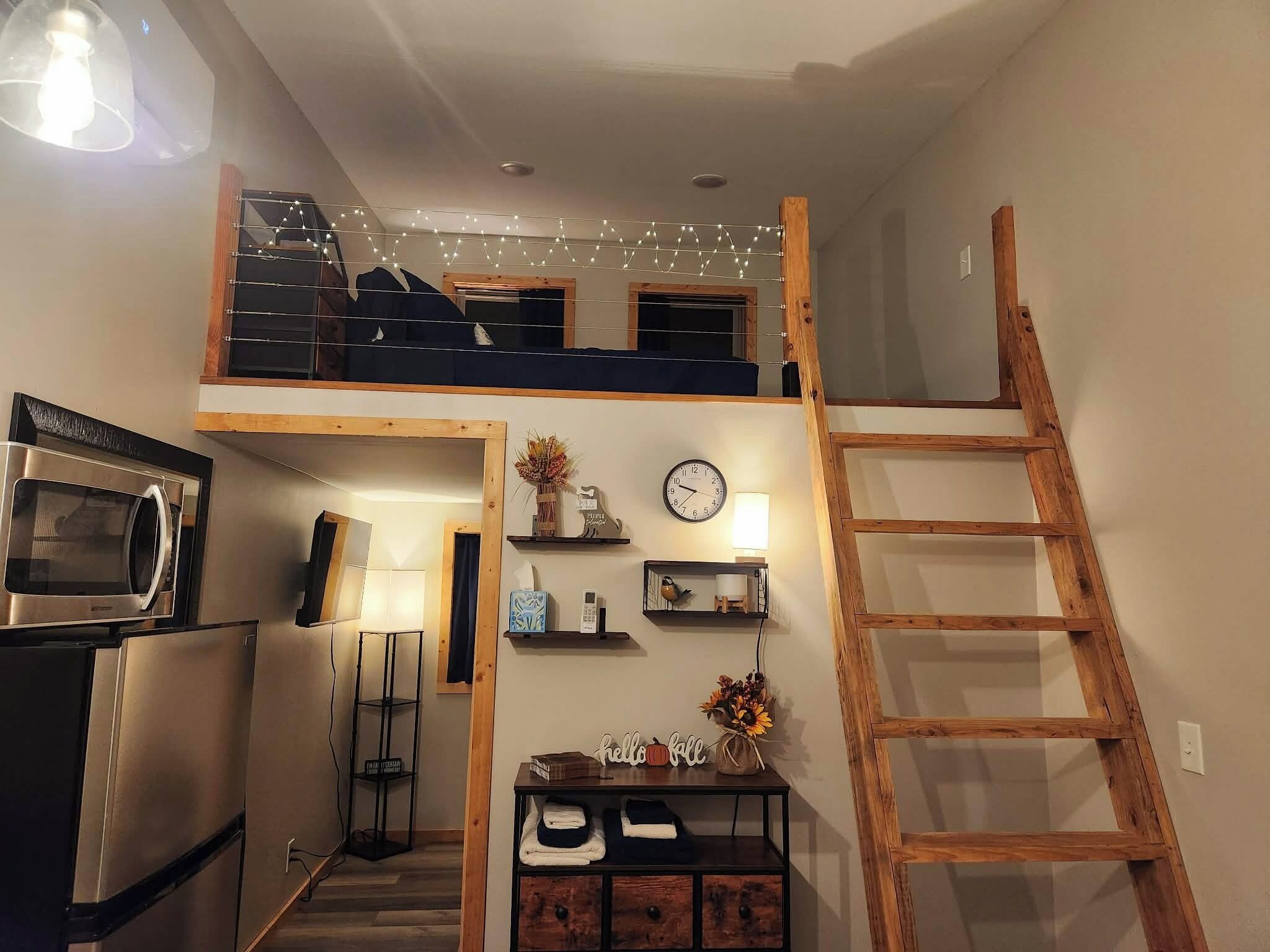 A loft-style room with a kitchenette, a wooden ladder, and a staircase.