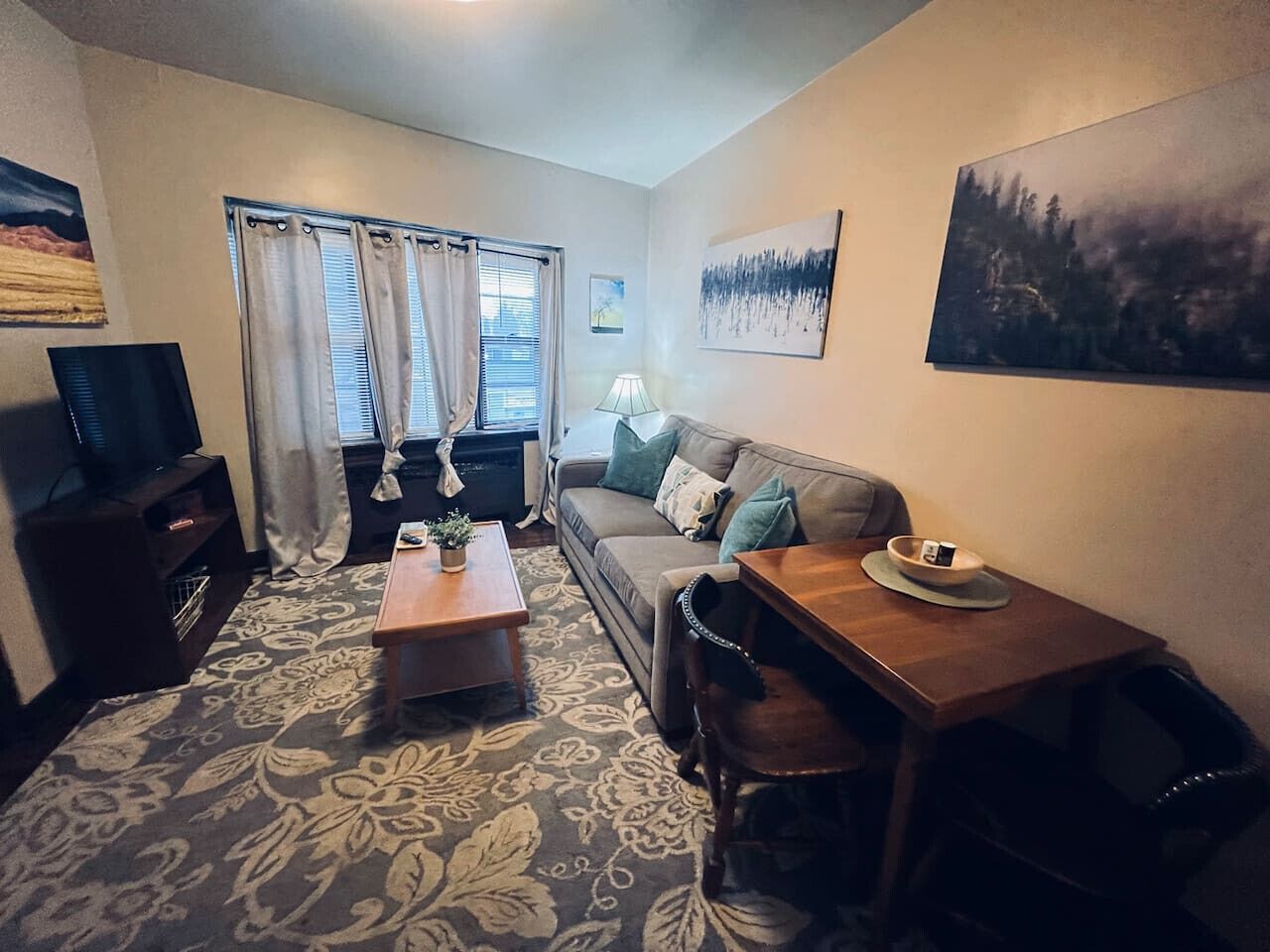 A compact living room with a sofa, a wooden table, a TV, and a patterned carpet.