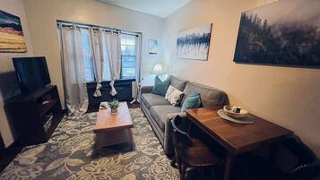 A compact living room with a sofa, a wooden table, a TV, and a patterned carpet.