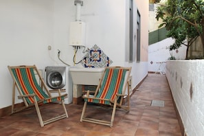 A small, enclosed outdoor area with two wooden chairs, a washing machine, and a tiled wall.