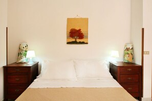 A bedroom with a bed, two nightstands, a wall-mounted painting, and two lamps.