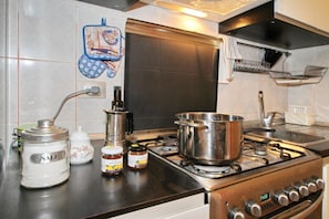 A kitchen with a stove, pots, a coffee maker, and jars of condiments.