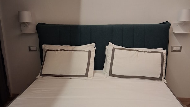 A neatly made bed with white linens and two pillows, a dark headboard, and two wall-mounted lamps on either side. - House Sant Angelo (Acquapendente)