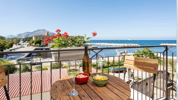 A balcony with a wooden table, a bottle of wine, and a bowl of snacks.