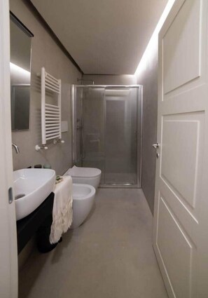 A narrow bathroom with a shower, a sink, and a toilet.
