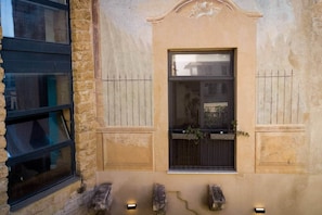 A building facade with a central window, stone walls, and a small window with plants. - The Ancient Arch | Boutique Apt w/ Private Terrace (Palermo)