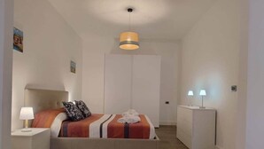 A bedroom with a bed, nightstands, a wardrobe, and a hanging light fixture. - Lollo's Terrace | Panoramic View | Mondello Beach (Palermo)