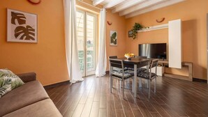 A living room with a sofa, a dining table with chairs, a TV, and a balcony with a sliding door. - nonMama | 2-Bath Stylish Apt near Mondello Beach (Palermo)