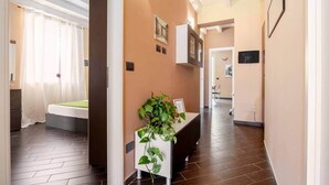 A hotel hallway with a reception desk, a bed with a green bedspread, and a plant on the desk. - nonMama | 2-Bath Stylish Apt near Mondello Beach (Palermo)