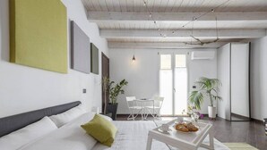A modern living room with a white sofa, a small coffee table, and a dining area with chairs and a table. - Mama | Your Stylish Oasis near Mondello Beach (Palermo)