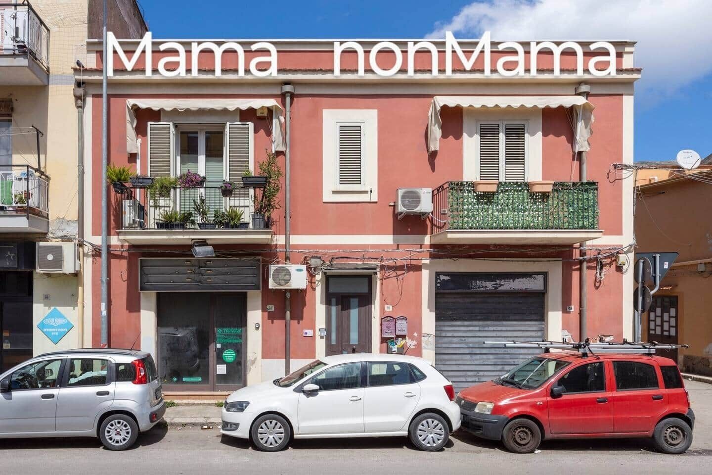 Un edificio con il cartello "Mama nonMama" e tre auto parcheggiate davanti.