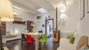 A modern living room with a sofa, a dining table with chairs, and a kitchen area in the background. - Mama | Your Stylish Oasis near Mondello Beach (Palermo)