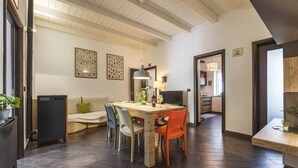 A dining area with a wooden table, chairs, and a black heater. There are framed botanical prints on the wall and a hanging light fixture. - Mama | Your Stylish Oasis near Mondello Beach (Palermo)