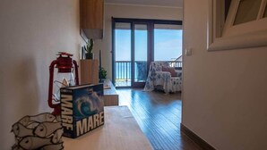 En hall som leder ut till en balkong med utsikt över havet, en brandsläckare och en låda märkt med texten ”Mare”.