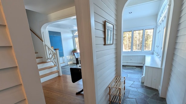 A spacious hallway with a wooden staircase, a blue patterned rug, and a view of a dining area with a table and chairs. - cozy home with mountain views. (Dorset)