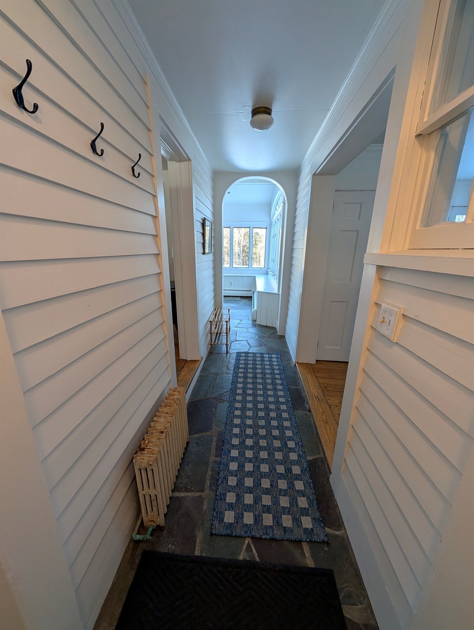 Un couloir étroit aux murs recouverts de lambris blancs, un tapis à motifs bleus et un radiateur.