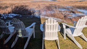 En vy över en gräsklädd äng med tre Adirondack-stolar som är placerade så att de vetter mot ett bergskedja.