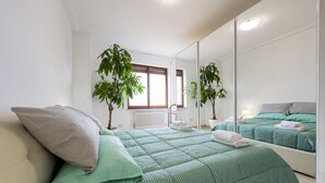 Une chambre à coucher avec un lit, un miroir, deux plantes en pot et une fenêtre.