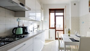 Une cuisine avec des meubles blancs, une cuisinière à gaz, une bouilloire et un coin repas avec une table dressée pour deux personnes.