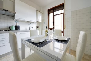A modern kitchen with white cabinets, a coffee maker, and a dining table set for two with plates, glasses, and a bottle.