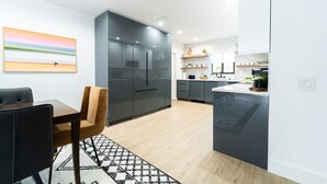 Eine moderne Küche mit dunklen Schränken, eine Essecke mit einem schwarzen Tisch und braunen Stühlen sowie ein großes Bild an der Wand.