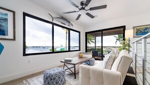 Ein modernes Wohnzimmer mit großem Fenster, Deckenventilator und Blick auf den Hafen.