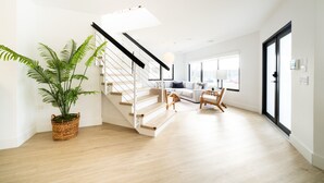 Ein modernes Interieur mit einer Treppe, einer Wohnbereiches mit Sofa und Sesseln sowie einem großen Fenster.