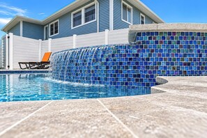 A swimming pool with a mosaic tile wall, a lounge chair, and a house in the background. - Sand Dollar Suite (Fort Myers Beach)
