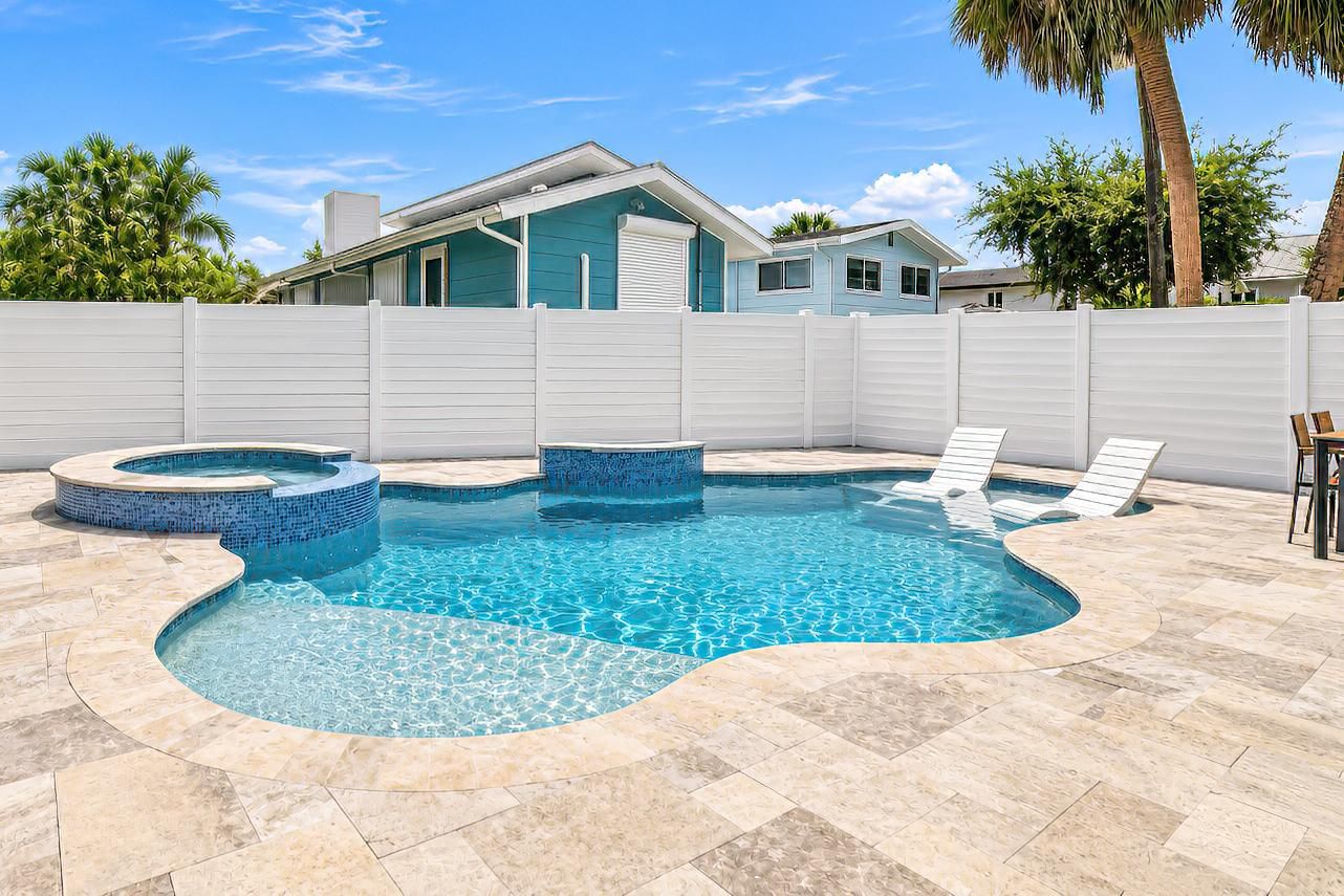 A swimming pool with a curved design, surrounded by a white fence, and a house in the background.