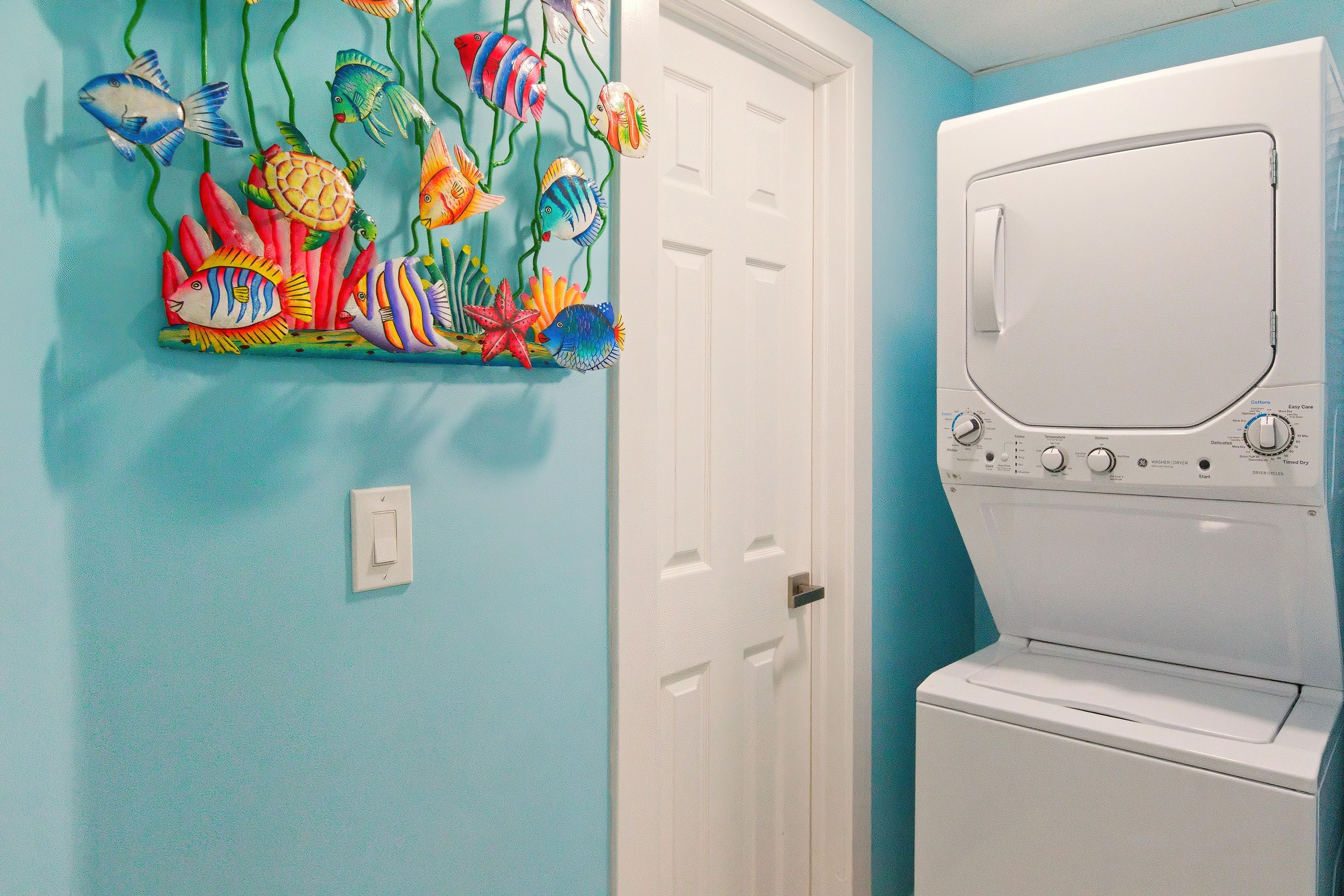 A laundry room with a white washer and dryer, a door, and a colorful fish mural on the wall.