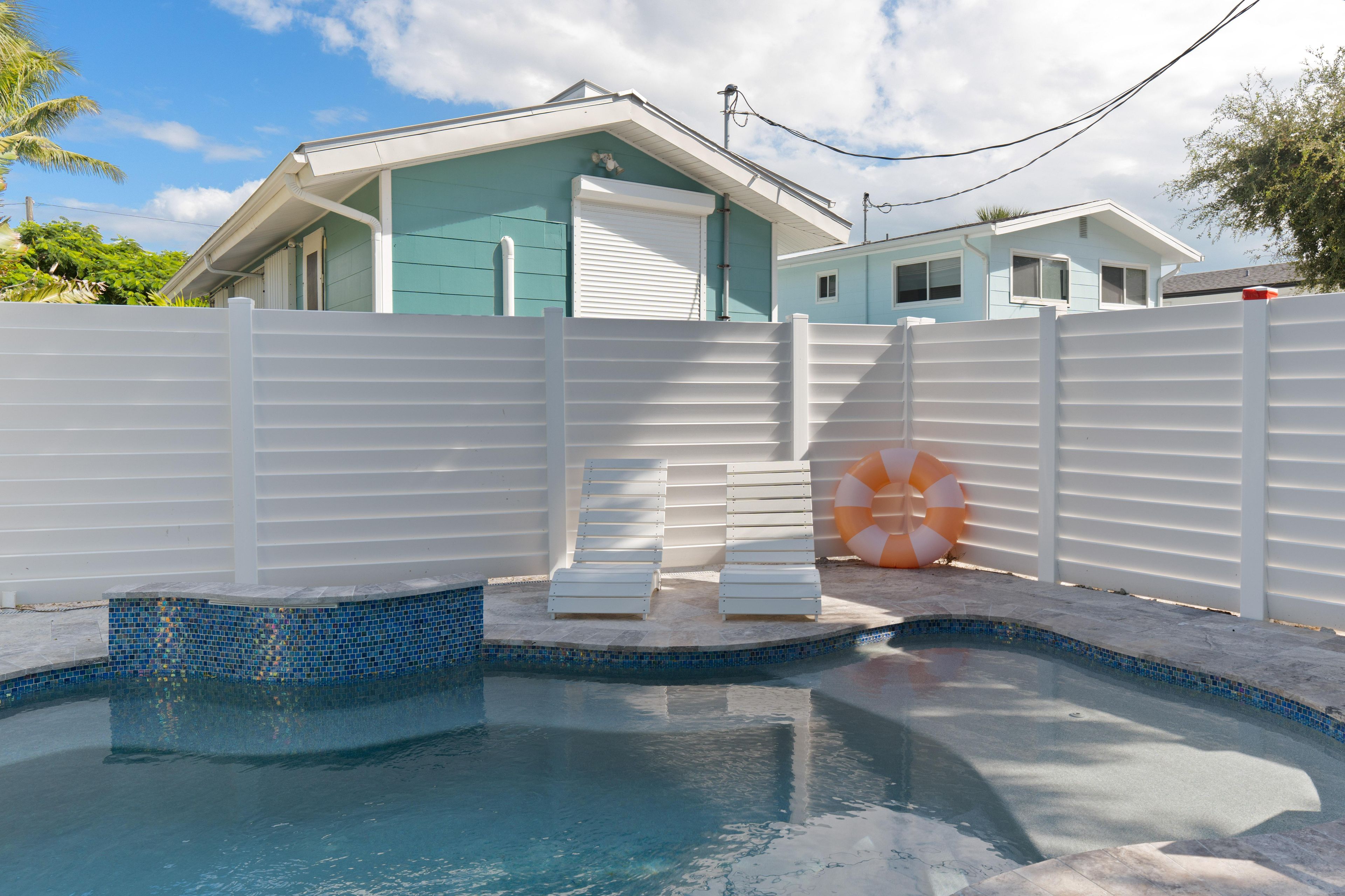 A swimming pool with a tiled edge, a white fence, and a lifebuoy.