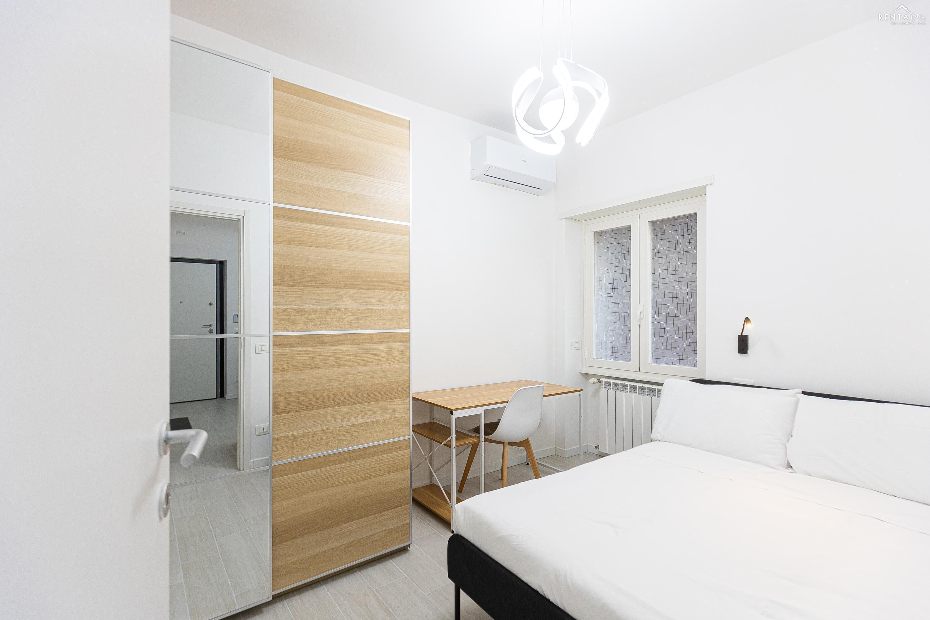 Ein modernes Schlafzimmer mit Bett, Schreibtisch und Stuhl. Ein Kleiderschrank mit Schiebetüren und ein Fenster mit Blick nach draußen.