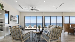 Un vaste salon offrant une vue imprenable sur l’océan, doté d’un ventilateur de plafond et aménagé dans un style moderne.