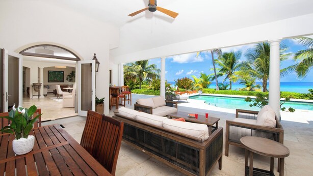 Un espacio de sala-comedor abierto con vista a la piscina, muebles de madera y un ventilador de techo.