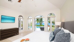 Un dormitorio espacioso con una cama grande, un aparador de madera oscura y vistas a una piscina y palmeras.