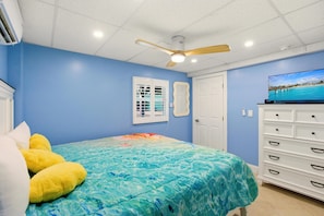 Une chambre à coucher avec un lit, un ventilateur de plafond, une télévision et une commode.