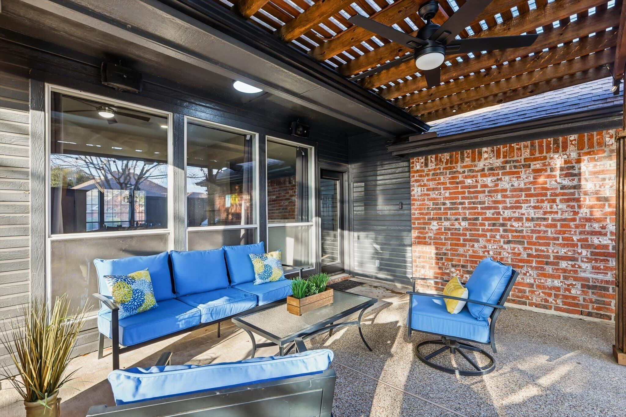 An outdoor patio with a blue sofa, a glass table, and a brick wall.