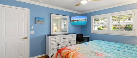 A bedroom with a bed, a dresser, a television, and a window with blinds.