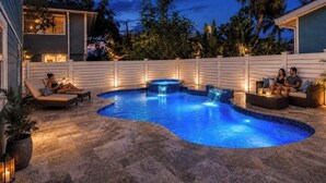 Una piscina con cascada, rodeada por una valla blanca y equipada con sillones de descanso y un jacuzzi.