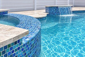 Piscina com azulejos de mosaico azul e borda de pedra.