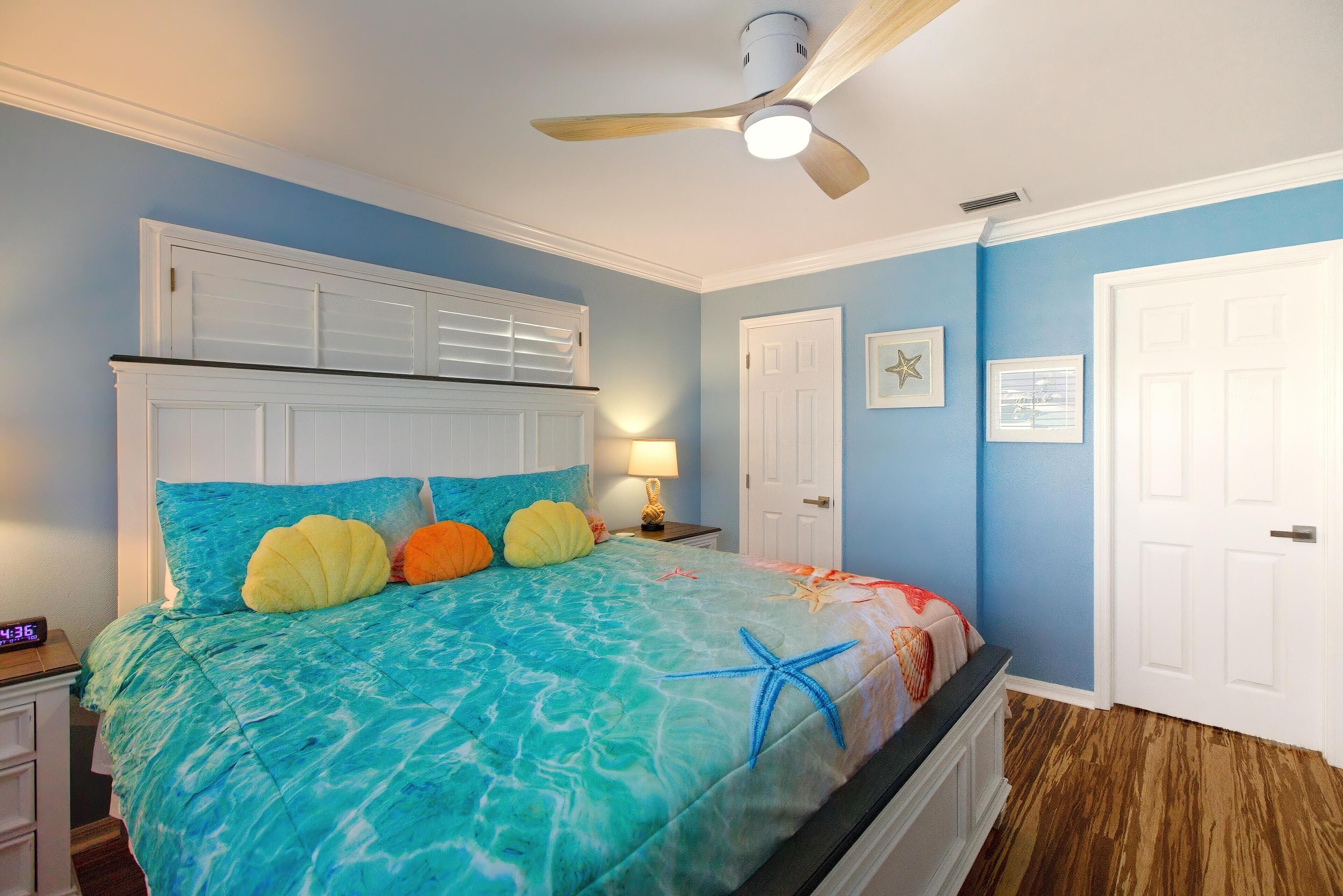A bedroom with a bed, a ceiling fan, a nightstand, and a wall clock.