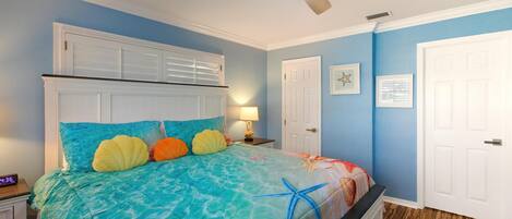 A bedroom with a bed, a ceiling fan, a nightstand, and a wall clock.